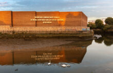 text on brick wall by river with ducks