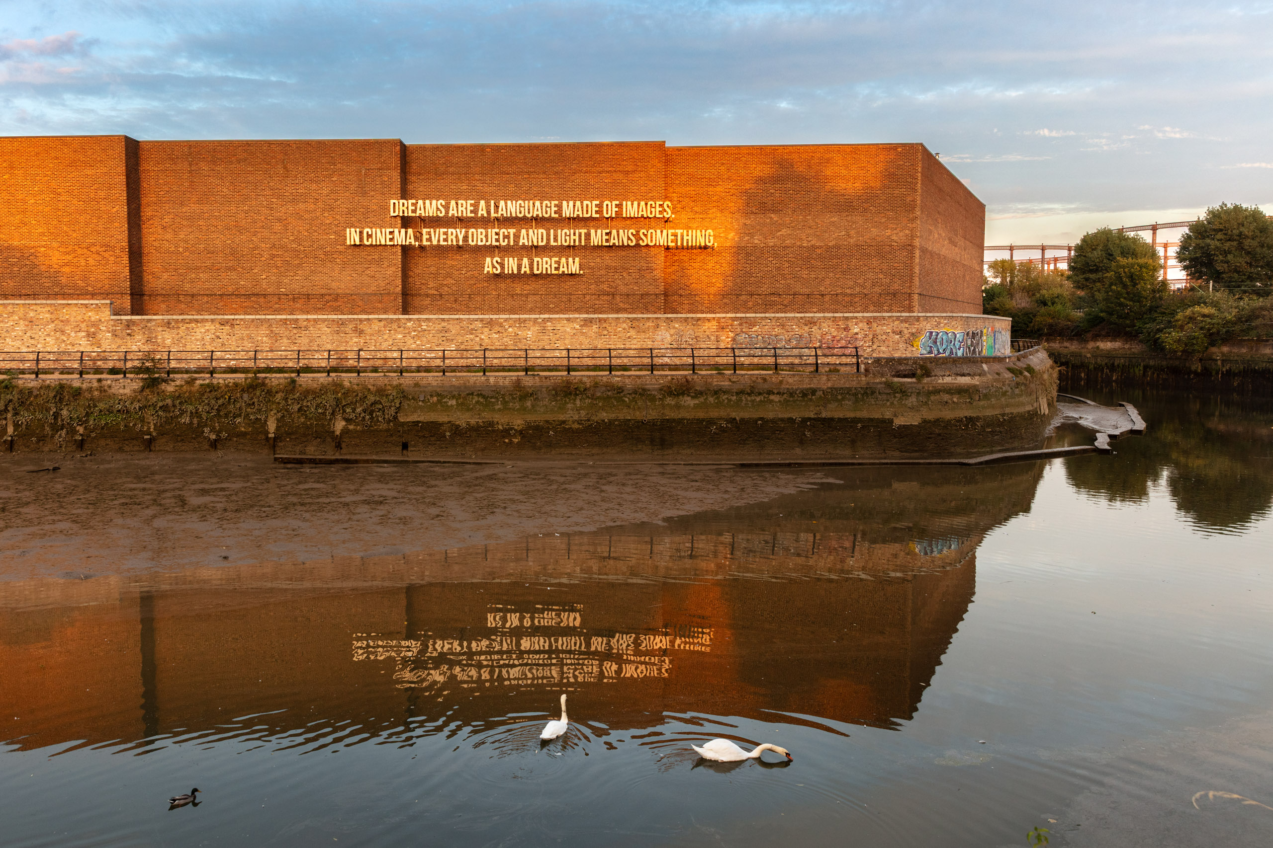 text on brick wall by river with ducks