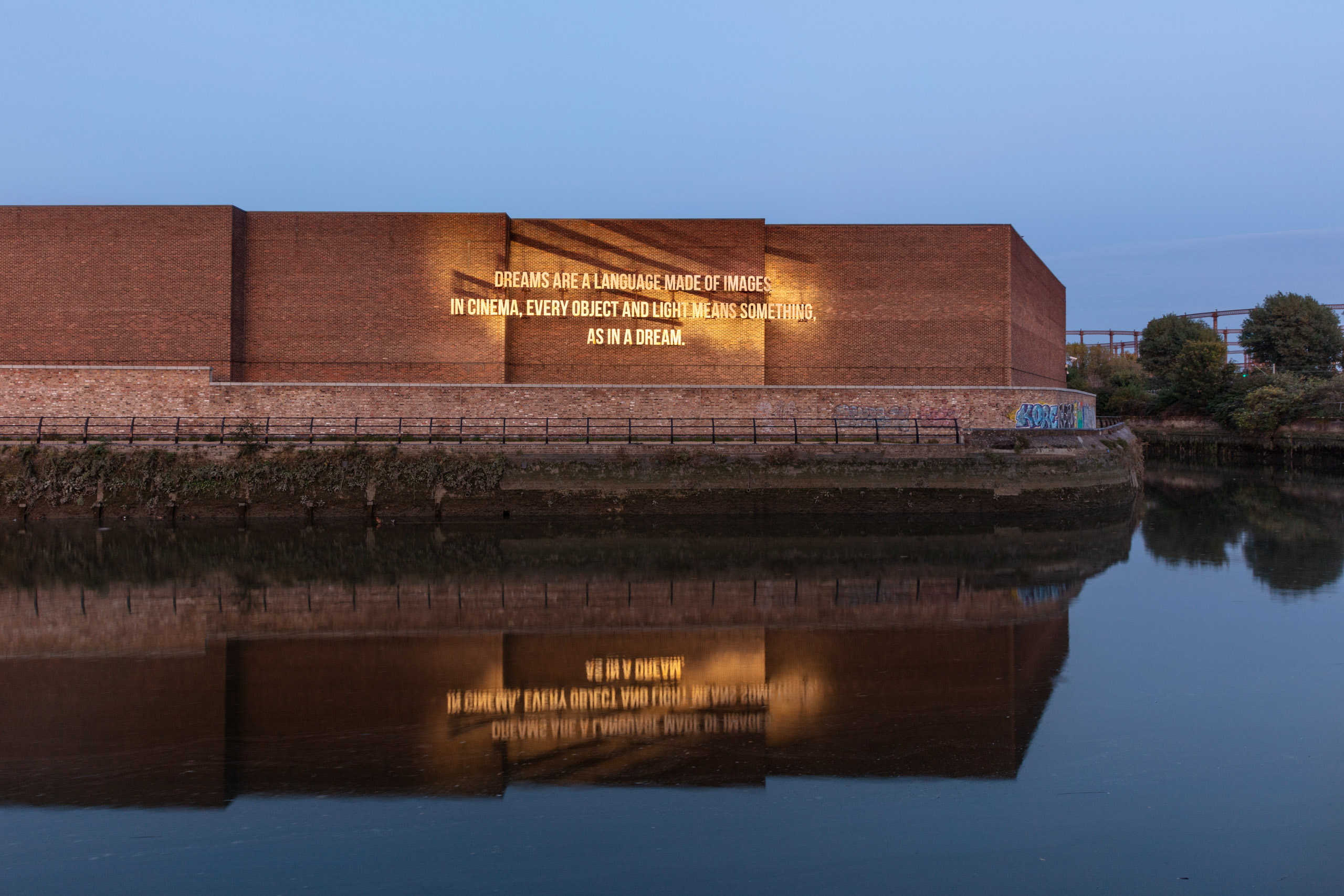 text on brick wall by river with ducks at night with reflection of letters on water