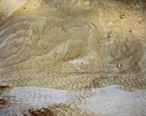 Sugar mounds in a warehouse with vehicle tracks on it combining to form a scale like pattern